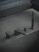Badarmatur in mattem Schwarz von Ideal Standard, bestehend aus vier Elementen: Wasserhahn, Wanneeinlauf und zwei Reglern, auf einer grauen Fläche platziert, vor horizontalen Jalousien.
